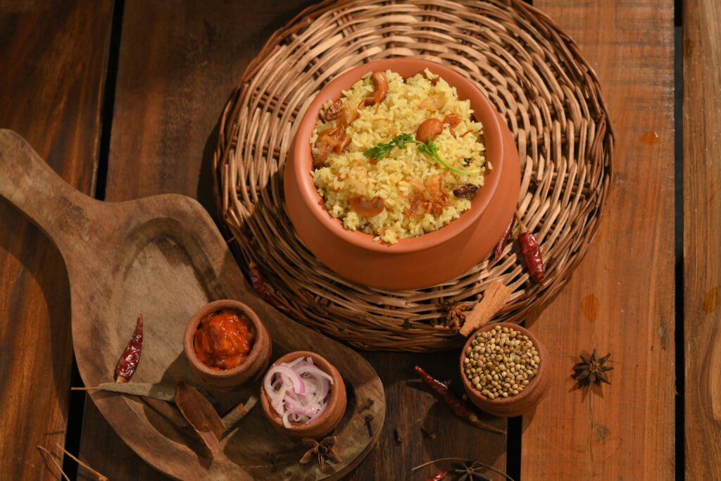Delicious South Indian biryani served in a traditional clay pot with side condiments on a wooden table.
